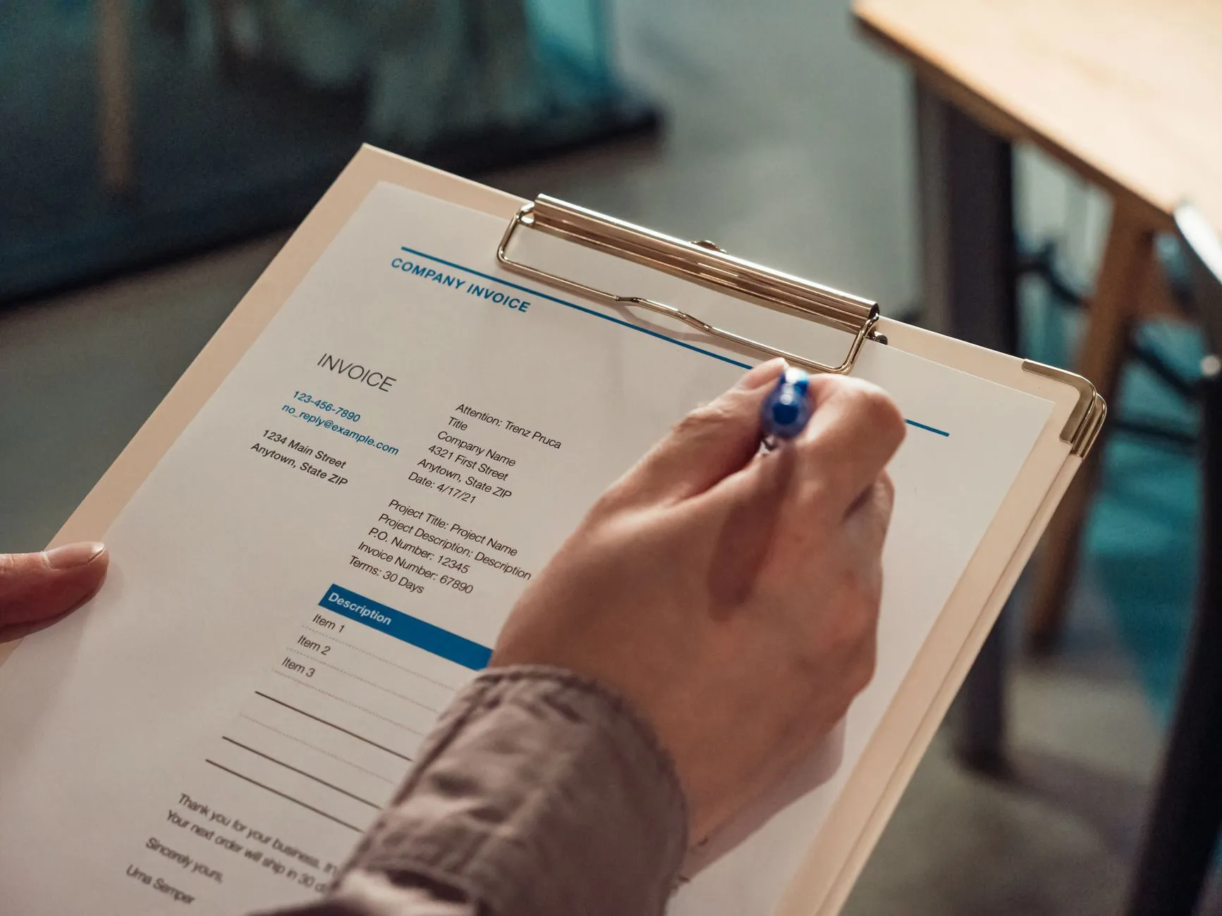 A hand signing a printed company invoice on a clipboard