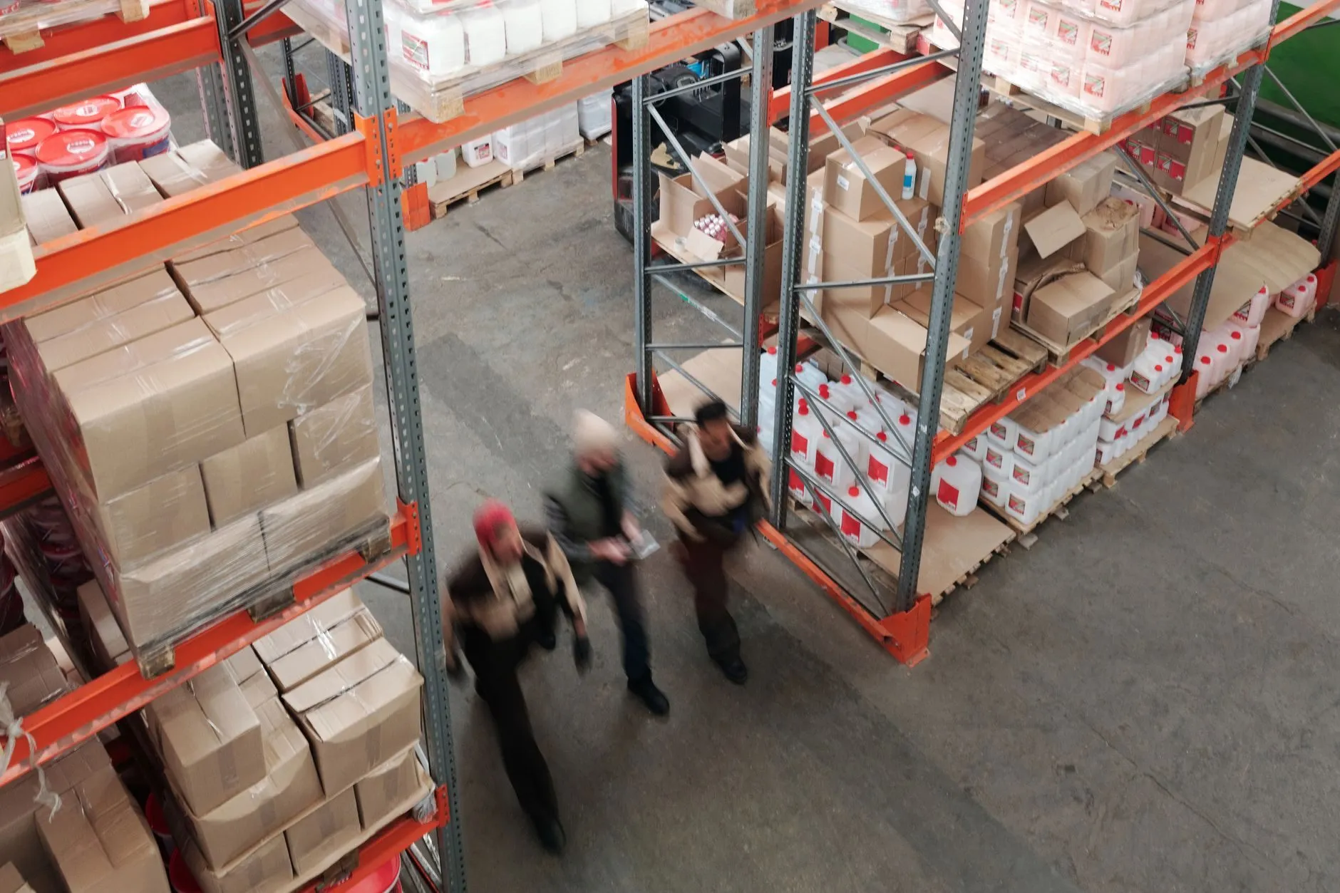Warehouse staff crossing an aisle between racking stacked with cartons, seen from above