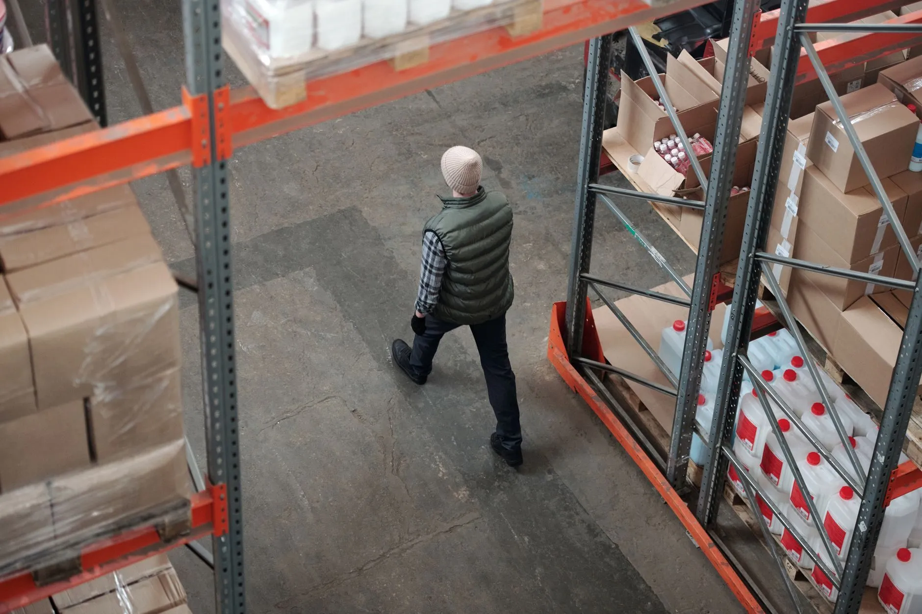 A person in a padded vest walking past racking stocked with cartons and bottles
