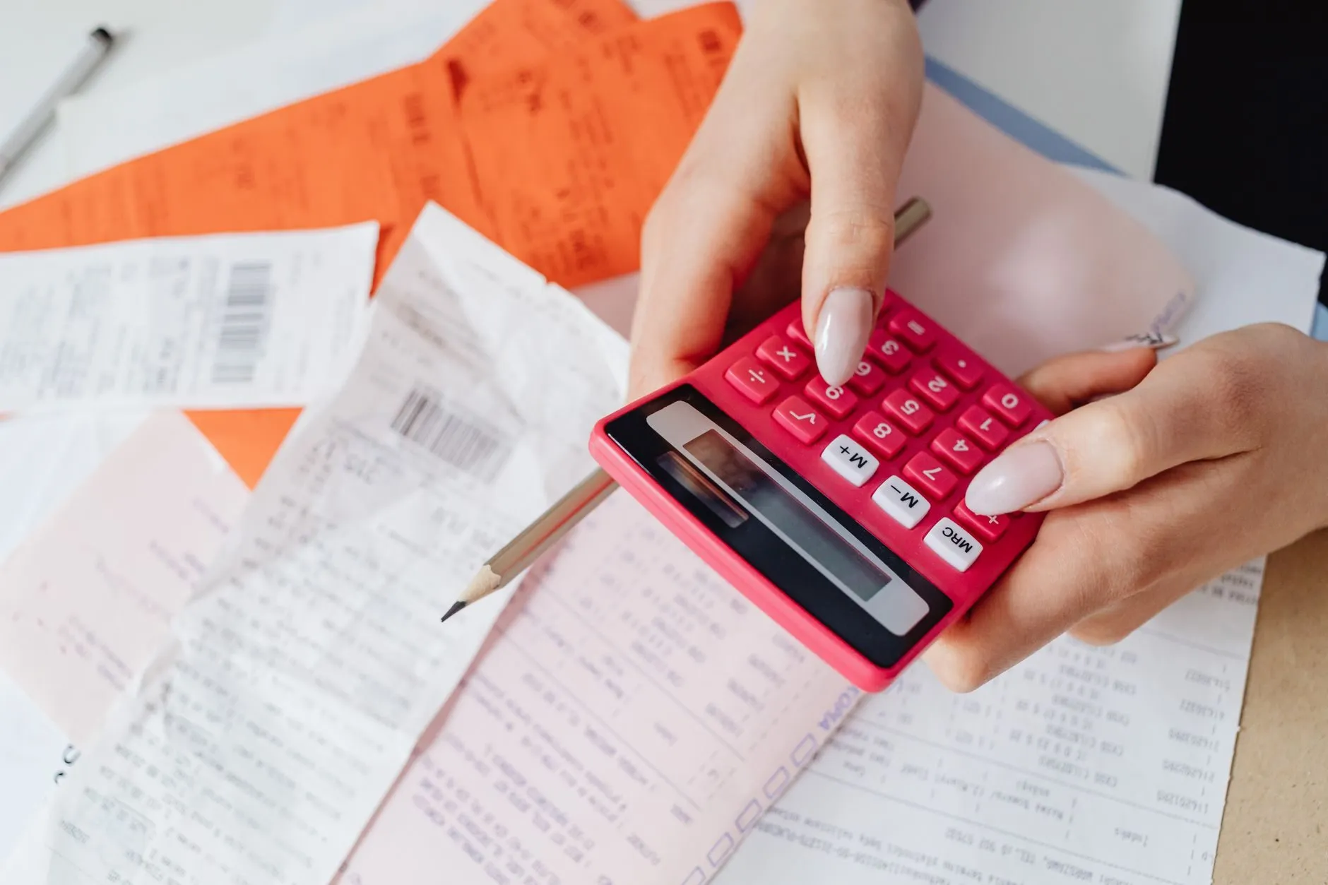 Hands working a pink calculator over a pile of supplier receipts and invoices