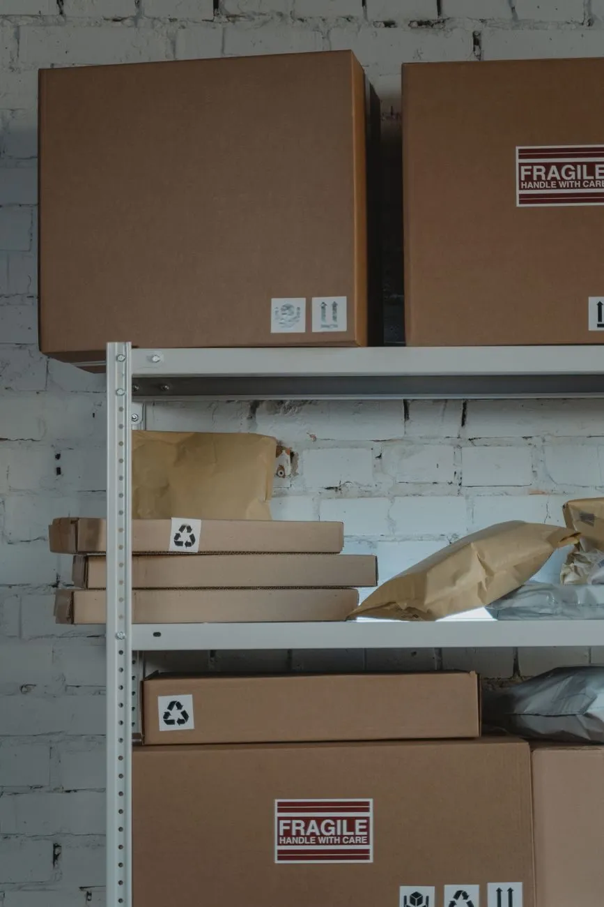 Cardboard parcels with fragile labels on metal shelving against a white brick wall